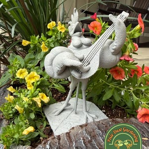 May include: A gray, textured garden statue of a chicken standing on a square base, playing a stringed instrument. The chicken has an open beak and is positioned among yellow and orange flowers. A logo with the text Pixie Dust Gardening is visible.