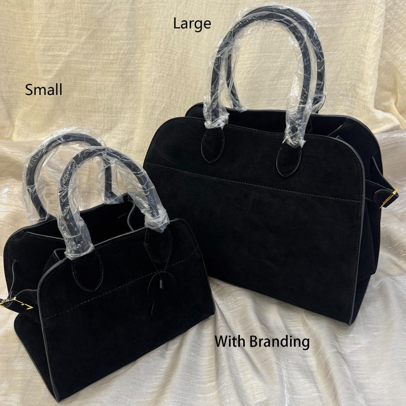 May include: Two black suede handbags, one large and one small, with rounded handles wrapped in plastic. The bags have a structured design and a top handle. The image includes the text "Large", "Small", and "With Branding".