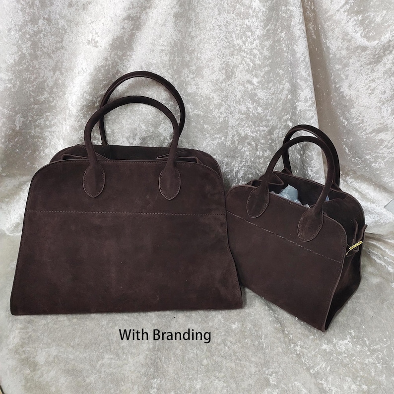 May include: Two brown suede handbags with rounded handles. The larger bag is rectangular, and the smaller bag is trapezoidal. Both bags have a soft, textured appearance and are set against a light-colored background. The text "With Branding" is at the bottom.