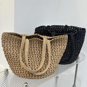 Può includere: Due borse tote aperte realizzate in materiale intrecciato. Una borsa è di colore marrone chiaro e l'altra è nera. Entrambe le borse presentano un motivo intrecciato spesso e strutturato su tutto il corpo e includono due manici abbinati.