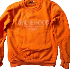 Könnte beinhalten: Orangefarbener Pullover mit dem Text "GOD IS GOOD" in Weiß, darunter die Worte "GIVE THANKS TO THE LORD FOR HE IS GOOD! PSALM 106:1".
