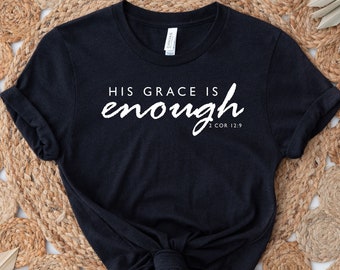 May include: Black t-shirt with white text that reads "His grace is enough 2 Cor 12:9". The shirt is laid out on a woven rug.