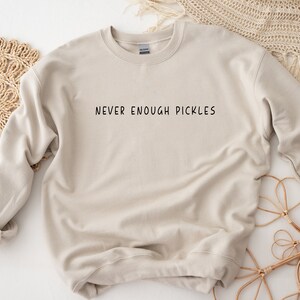 K&ouml;nnte beinhalten: Ein hellbeiger Pullover mit dem Aufdruck "NEVER ENOUGH PICKLES" in Schwarz auf der Vorderseite.