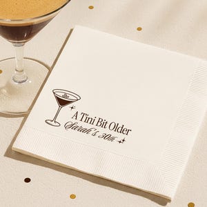 Personalized espresso martini themed custom 30th birthday cocktail napkin featuring A Tini Bit Older design with name and age. Elegant neutral napkin displayed on a warm tabletop, perfect for milestone birthday celebrations, stylish party décor, and modern bar settings.