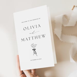 Może przedstawiać: Karta zaproszenia na ślub z prostym wzorem, przedstawiająca imiona Olivia i Matthew, małą ilustrację kwiatową i datę 26 września 2026.