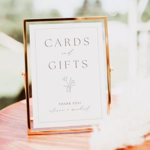 May include: A white sign with a gold frame that says "Cards and Gifts" with a simple floral design and the text "Thank You! Oliver + Michael".