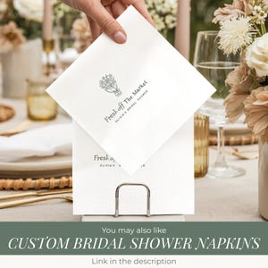 Puede incluir: Servilletas de papel blancas con un dise&ntilde;o floral y el texto "Fresh off The Market, Olivia's Bridal Shower". Las servilletas se muestran en un servilletero plateado. La imagen tambi&eacute;n incluye el texto "Custom Bridal Shower Napkins".