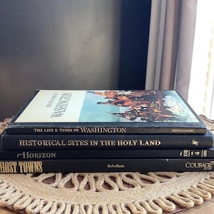 May include: A stack of four hardcover books with black covers and gold lettering. The titles are "The Life & Times of Washington", "Historical Sites in the Holy Land", "Horizon", and "Ghost Towns".