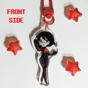 K&ouml;nnte beinhalten: Ein durchsichtiger Acryl-Schl&uuml;sselanh&auml;nger mit einer Cartoon-Anime-Figur mit schwarzen Haaren, einem rot-schwarzen Outfit und einer rot-schwarzen Gesichtsmaske. Der Schl&uuml;sselanh&auml;nger hat einen roten Metallverschluss. Der Hintergrund ist wei&szlig; mit drei roten sternf&ouml;rmigen Objekten.
