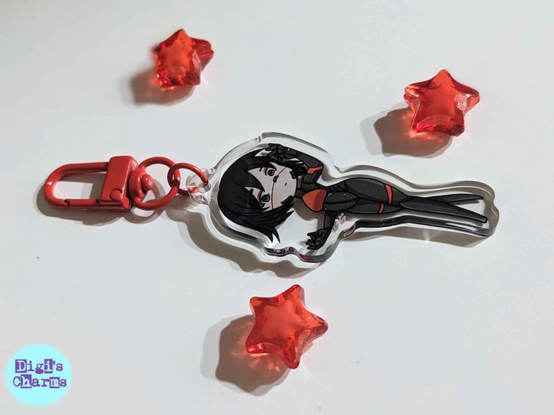 K&ouml;nnte beinhalten: Ein durchsichtiger Acryl-Schl&uuml;sselanh&auml;nger mit einer Comicfigur mit schwarzen Haaren, einem rot-schwarzen Outfit und einem roten Augenpflaster. Der Schl&uuml;sselanh&auml;nger hat einen silbernen Metallring und einen roten Metallverschluss.