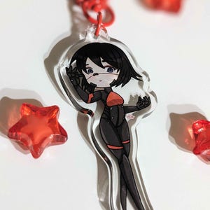 K&ouml;nnte beinhalten: Ein durchsichtiger Acryl-Schl&uuml;sselanh&auml;nger mit einer Cartoon-Anime-Figur mit schwarzen Haaren, einem rot-schwarzen Outfit und einer wei&szlig;en Gesichtsmaske. Die Figur steht mit einer erhobenen Hand. Der Schl&uuml;sselanh&auml;nger ist von roten sternf&ouml;rmigen Objekten umgeben.