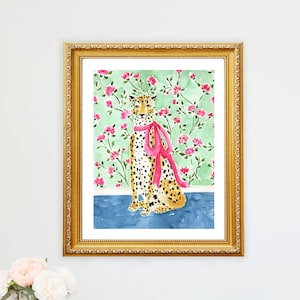 May include: A framed watercolor painting of a cheetah wearing a pink ribbon. The cheetah is sitting on a blue background with a green and pink floral pattern behind it.