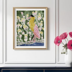 May include: A framed watercolor print featuring a bird with yellow and pink plumage, set against a green floral background. The artwork is displayed above a navy blue dresser with gold accents, complemented by a vase of pink flowers.