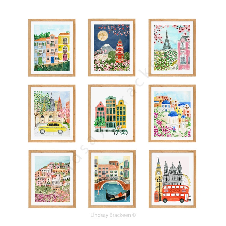 May include: A collection of nine framed watercolor art prints depicting various global cityscapes and landmarks, including scenes of Paris, London, New York, Venice, Santorini, and Japan, all presented in light wood frames arranged in a grid.