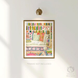 May include: Watercolour print depicting a reading nook with a bookshelf, sofa, and patterned rug. The artwork has a gold frame and a warm colour palette of pinks, greens, and oranges. The text "*FRAME NOT INCLUDED" is visible at the bottom.