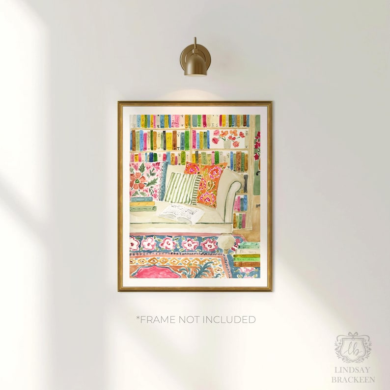 May include: Watercolour print depicting a reading nook with a bookshelf, sofa, and patterned rug. The artwork has a gold frame and a warm colour palette of pinks, greens, and oranges. The text "*FRAME NOT INCLUDED" is visible at the bottom.