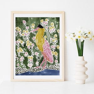 May include: Watercolor print of a bird with yellow and pink plumage, set against a backdrop of green foliage and yellow and pink flowers. The artwork is framed in a light wood frame, creating a decorative piece for home decor.