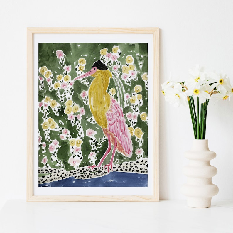 May include: Watercolor print of a bird with yellow and pink plumage, set against a backdrop of green foliage and yellow and pink flowers. The artwork is framed in a light wood frame, creating a decorative piece for home decor.