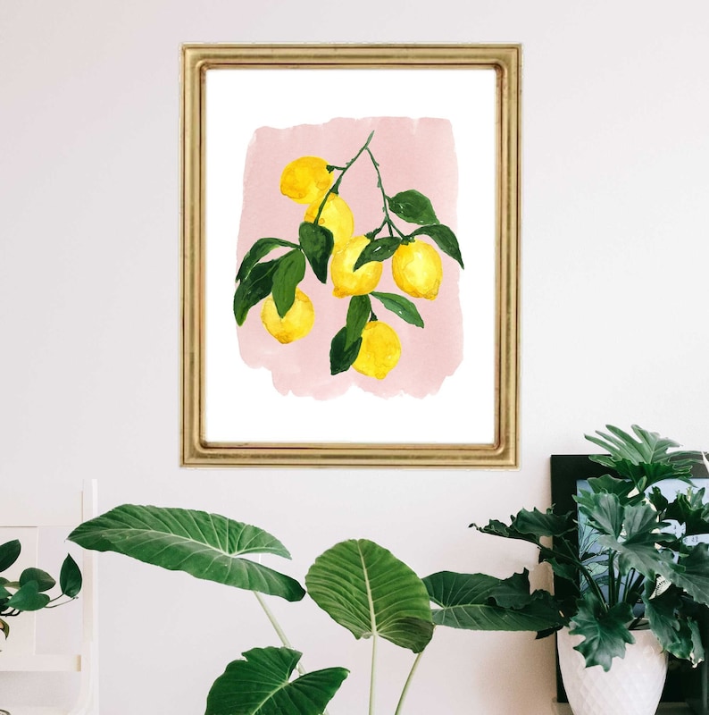 May include: A framed watercolor print featuring a branch of lemons with green leaves against a pink background. The artwork is displayed in a gold-colored frame, adding a touch of elegance to the botanical theme.