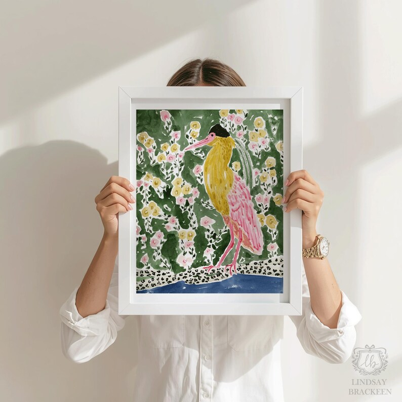 May include: A framed watercolor print featuring a bird with yellow and pink plumage, set against a floral background. The artwork is held by a person, showcasing the vibrant colors and artistic style. The print is signed by Lindsay Brackeen.