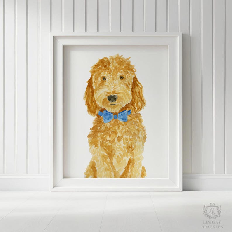 May include: A framed watercolor painting of a golden-brown dog with curly fur, wearing a bright blue bow tie around its neck. The dog is depicted in a front-facing portrait style, centered within a white frame against a white background.