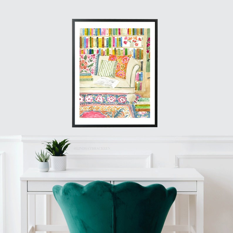 May include: Watercolour painting of a reading nook. A white armchair with floral and striped cushions. A bookshelf filled with colourful books is in the background. A patterned rug and open book complete the scene.