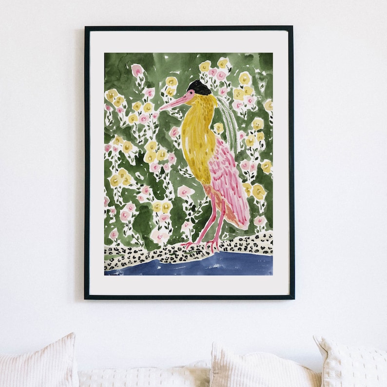 May include: Framed watercolor print of a bird with yellow and pink plumage, black head, and long beak. The bird stands on a leopard-print surface above a blue area, set against a backdrop of green foliage and yellow and pink flowers.