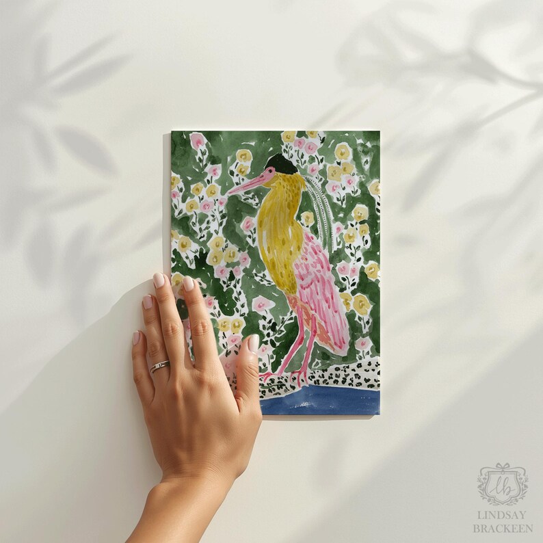 May include: Watercolor painting of a bird with yellow and pink plumage, set against a floral background of yellow and pink flowers on a green backdrop. The bird is standing on a blue and black patterned base. The artist's signature is in the bottom right corner.