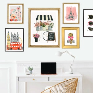 May include: A white desk with a laptop, a lamp, and a potted plant. Above the desk are nine framed prints with various images, including a flower cart, the Eiffel Tower, and a red double-decker bus. The text "@lindsaybracken" is written on the wall.