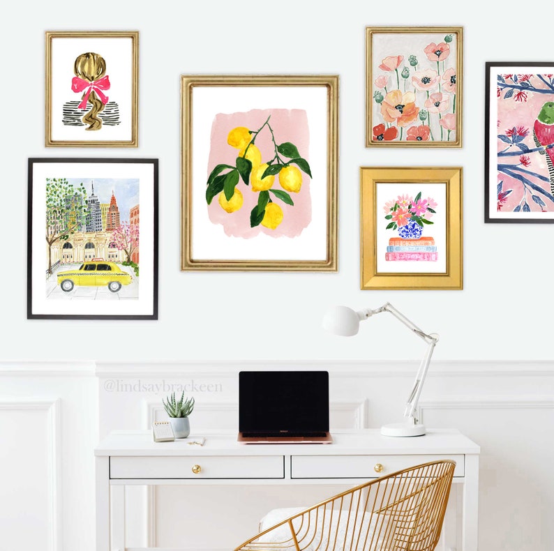 May include: A collection of framed watercolor art prints. The prints feature a variety of subjects, including a lemon branch, flowers, a New York City scene with a yellow taxi, and a portrait of a girl with a pink bow. The frames are gold and black.