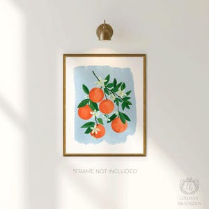 K&ouml;nnte beinhalten: Ein gerahmter Kunstdruck mit einer Aquarellillustration von Orangen auf einem Ast mit gr&uuml;nen Bl&auml;ttern und wei&szlig;en Bl&uuml;ten vor einem hellblauen Hintergrund. Der Rahmen ist goldfarben. Der Text unten lautet "FRAME NOT INCLUDED".