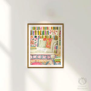 May include: Watercolour print depicting a comfortable reading space, featuring a bookshelf with vibrant books. A white sofa with patterned cushions rests on a floral rug. The artwork is framed in a gold-coloured frame.