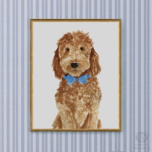 May include: A watercolor painting of a golden-brown curly-haired dog wearing a bright blue bow tie. The dog is centered against a light gray background, and the entire artwork is enclosed within a thin, metallic gold-colored rectangular frame.