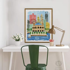 May include: A framed watercolor print of a city skyline featuring a prominent domed building, a red ferris wheel, and various skyscrapers in shades of red, yellow, and blue, set against a light blue sky above a dark blue body of water.