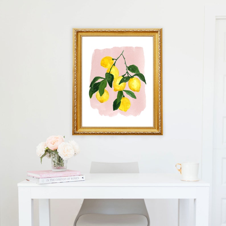 May include: A framed watercolor print featuring a lemon branch with bright yellow lemons and green leaves against a pink background. The gold frame adds a touch of elegance to the botanical artwork, suitable for kitchen or dining room decor.