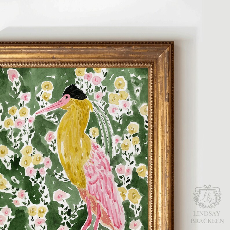 May include: Watercolor painting of a bird with yellow and pink plumage, set against a green floral background with pink and yellow flowers. The artwork is framed in a gold-colored ornate frame. The artist's signature is in the bottom right corner.