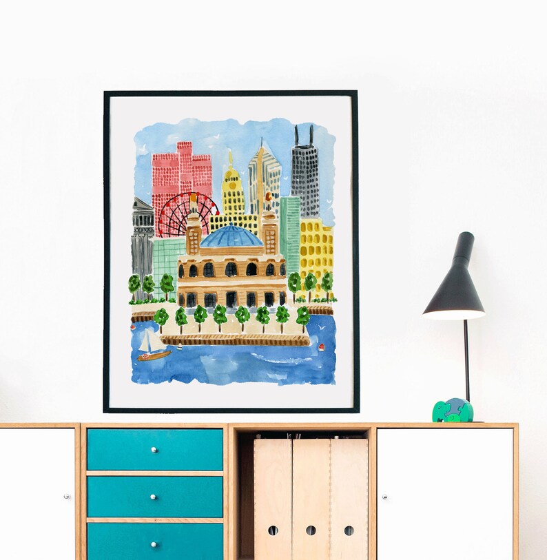 May include: A framed watercolor print depicting a city skyline with a prominent domed building in the foreground, a red Ferris wheel, and various skyscrapers in shades of red, yellow, and gray, set against a blue sky and water with a small sailboat.
