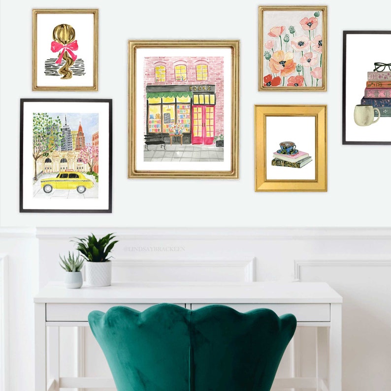 May include: A collection of framed watercolor art prints. The prints feature various subjects, including a New York City street scene with a yellow taxi, a bookstore facade, and floral arrangements. The frames are gold and black, and the overall aesthetic is artistic and decorative.
