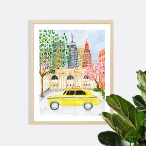 May include: A framed watercolor print depicting a yellow taxi cab on a city street in front of a large building with arched windows. The background features tall skyscrapers, a green tree, and a pink flowering tree under a light blue sky.
