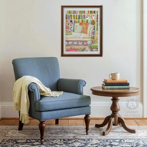 May include: A comfortable interior scene with a blue armchair and a cream-coloured throw. A small, round wooden side table holds books and a mug. A framed artwork shows a colourful bookshelf. The scene evokes a sense of relaxation.