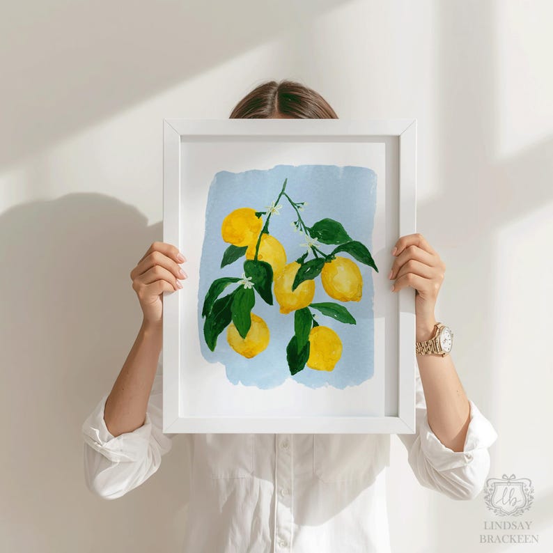 K&ouml;nnte beinhalten: Ein gerahmter Aquarelldruck mit einem Zitronenzweig mit leuchtend gelben Zitronen und gr&uuml;nen Bl&auml;ttern vor einem hellblauen Hintergrund. Das Kunstwerk wird von einer Person gehalten, die ein wei&szlig;es Hemd tr&auml;gt.