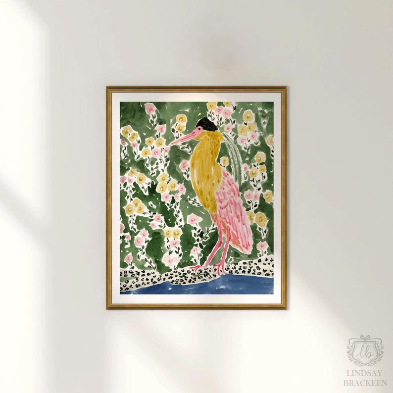 May include: A framed watercolor print featuring a bird with yellow and pink plumage, set against a backdrop of green foliage and yellow and pink flowers. The bird stands on a blue and leopard print border. The artwork is signed by Lindsay Brackeen.