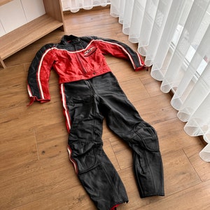 May include: A red and black leather motorcycle racing suit with white stripes and a logo on the chest.