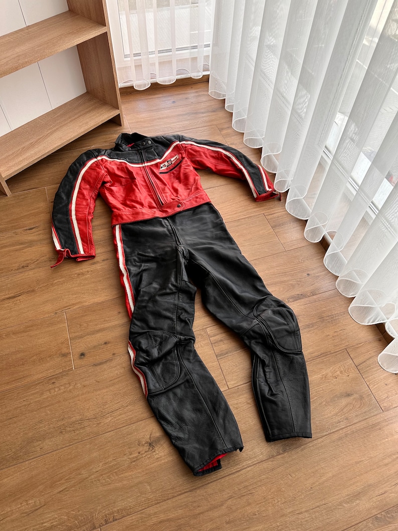 May include: A red and black leather motorcycle racing suit with white stripes and a logo on the chest.