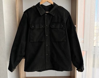 Puede incluir: Una camisa negra de manga larga con cierre de botones y dos bolsillos grandes. La camisa tiene un parche en el pecho izquierdo que dice "SECURITY".