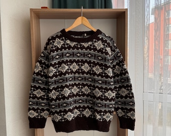 May include: A brown sweater with a white and blue geometric pattern. The sweater is hanging on a wooden shelf.