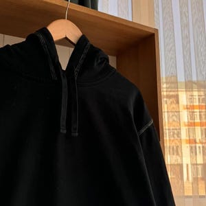 Pu&ograve; includere: Una felpa con cappuccio nera con coulisse e un sottile dettaglio di cuciture a contrasto.