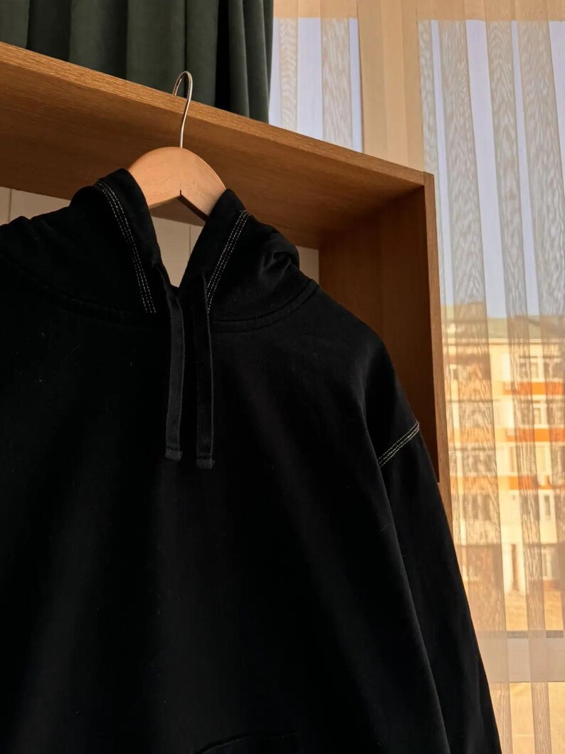 Pu&ograve; includere: Una felpa con cappuccio nera con coulisse e un sottile dettaglio di cuciture a contrasto.