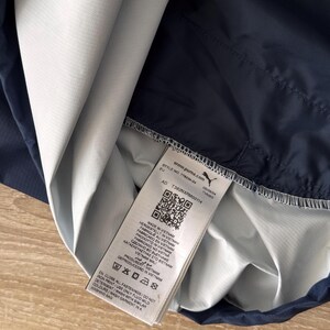 May include: A navy blue and white athletic jacket with a tag that includes the text "www.puma.com" and "MADE IN VIETNAM". The jacket is partially folded, revealing the interior lining.