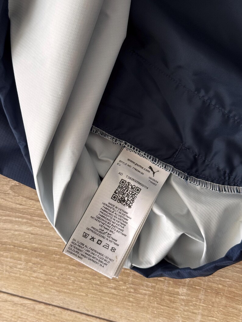 May include: A navy blue and white athletic jacket with a tag that includes the text "www.puma.com" and "MADE IN VIETNAM". The jacket is partially folded, revealing the interior lining.